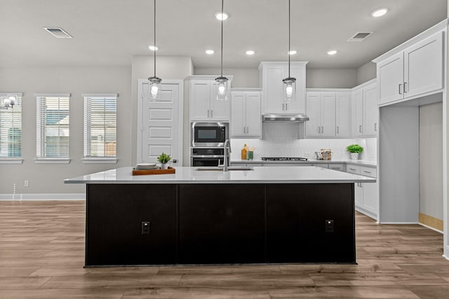 kitchen featuring built in microwave, white cabinetry, a kitchen island with sink, and pendant lighting