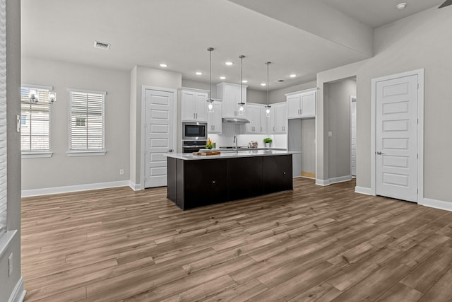 kitchen with pendant lighting, white cabinets, stainless steel appliances, a center island with sink, and light hardwood / wood-style flooring