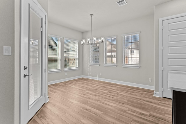 unfurnished dining area with a notable chandelier and light wood-type flooring