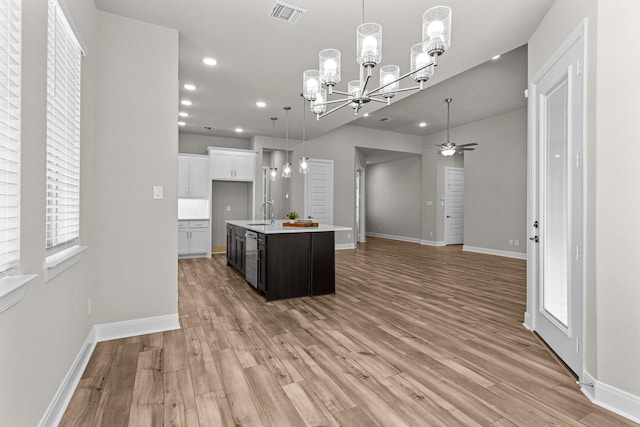 kitchen featuring sink, hanging light fixtures, white cabinets, a center island with sink, and light wood-type flooring