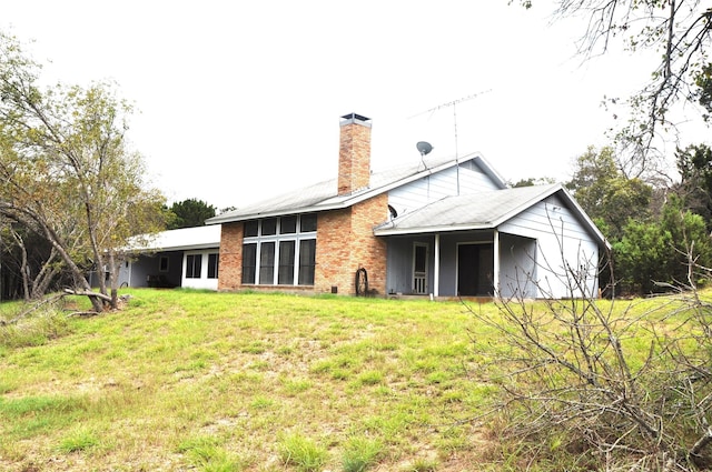 rear view of house with brick siding, a lawn, and a chimney