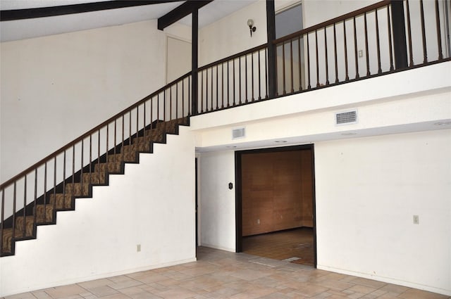 stairway with high vaulted ceiling, visible vents, baseboards, beam ceiling, and stone finish flooring