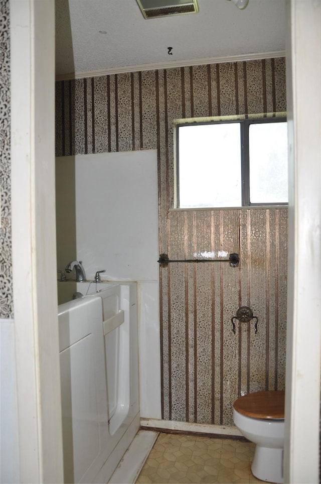 bathroom featuring toilet, washer / dryer, a washtub, and visible vents