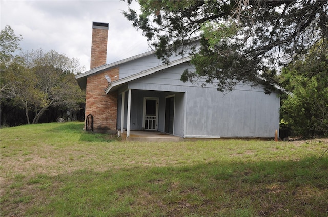 rear view of house with brick siding, a chimney, and a yard