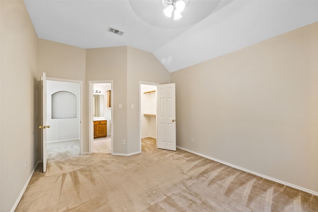 unfurnished bedroom with a closet, lofted ceiling, a spacious closet, light colored carpet, and ensuite bathroom