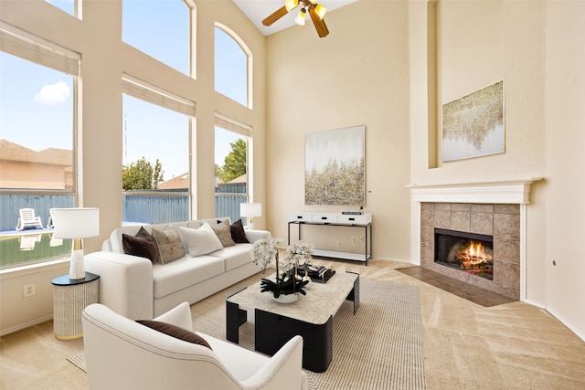 carpeted living room with ceiling fan, a tiled fireplace, and high vaulted ceiling