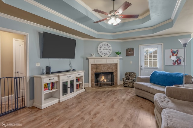 living room featuring a raised ceiling, a fireplace, ornamental molding, ceiling fan, and light wood-type flooring