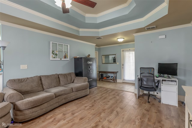 living room featuring light wood-type flooring, crown molding, a tray ceiling, and ceiling fan