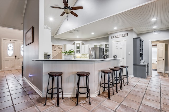 kitchen with a kitchen breakfast bar, stainless steel fridge, kitchen peninsula, ceiling fan, and white cabinets