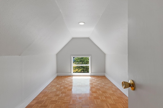 additional living space featuring a textured ceiling, vaulted ceiling, and light parquet flooring