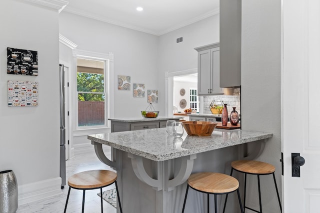 kitchen with kitchen peninsula, a kitchen bar, gray cabinets, and light stone countertops