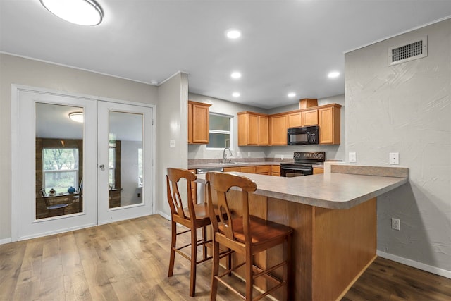 kitchen featuring black appliances, hardwood / wood-style floors, a breakfast bar, kitchen peninsula, and sink