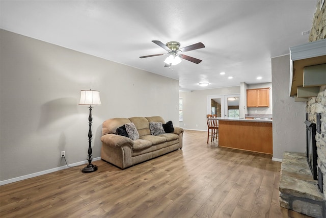 living room featuring light wood-type flooring, ceiling fan, and a stone fireplace