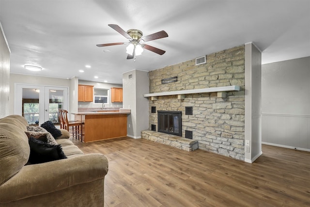 living room with french doors, hardwood / wood-style floors, sink, a stone fireplace, and ceiling fan