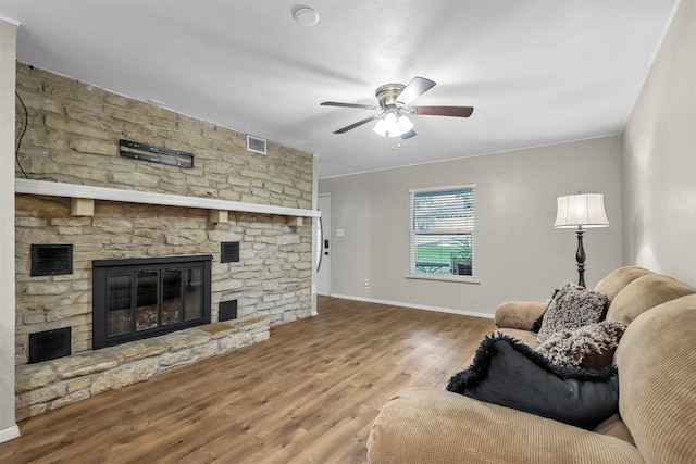 living room featuring ceiling fan, wood-type flooring, and a stone fireplace