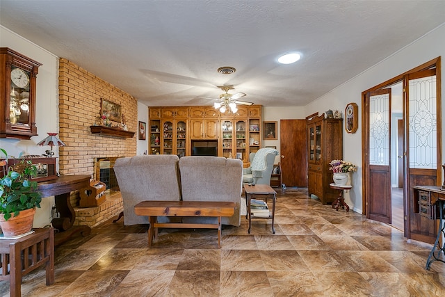 living room with ceiling fan, a textured ceiling, and a brick fireplace