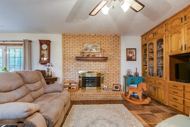 living room with ceiling fan, a fireplace, and a textured ceiling