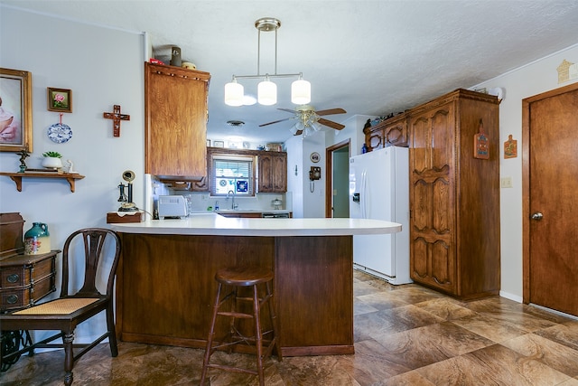 kitchen featuring white refrigerator with ice dispenser, kitchen peninsula, sink, ceiling fan, and hanging light fixtures