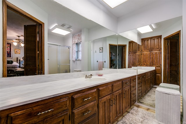 bathroom featuring a skylight, tile patterned flooring, a shower with shower door, ceiling fan, and vanity