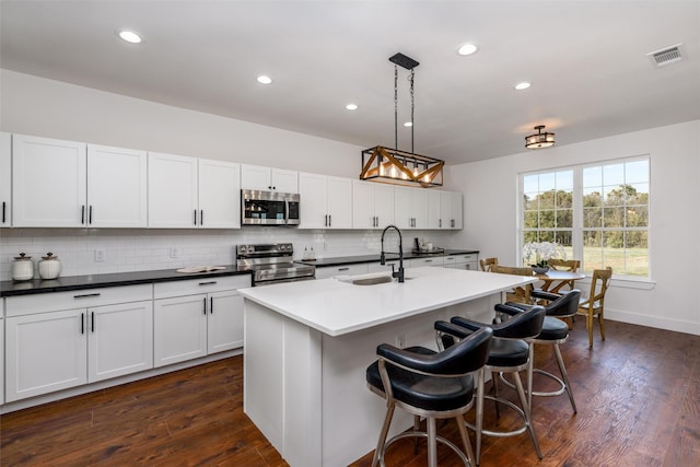 kitchen with sink, stainless steel appliances, white cabinets, a center island with sink, and decorative light fixtures