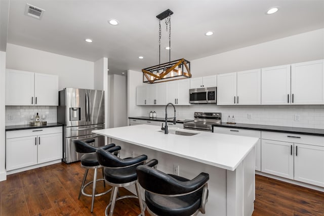 kitchen with pendant lighting, sink, appliances with stainless steel finishes, a kitchen island with sink, and white cabinets