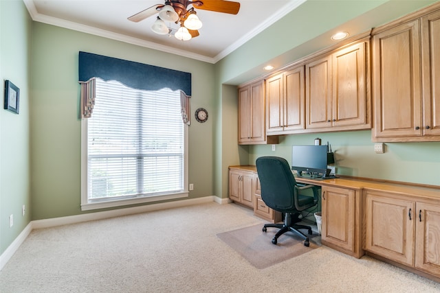 carpeted office space with built in desk, ceiling fan, and crown molding