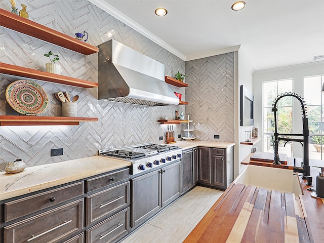 kitchen with wall chimney exhaust hood, dark brown cabinets, stainless steel gas cooktop, backsplash, and ornamental molding