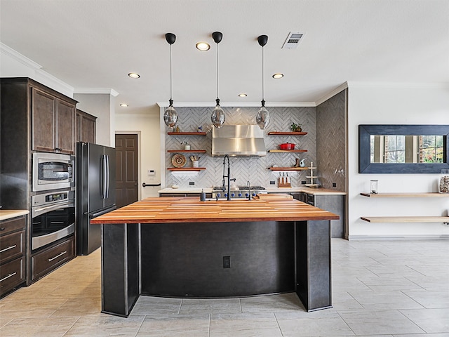 kitchen with dark brown cabinets, a center island with sink, extractor fan, stainless steel appliances, and butcher block counters