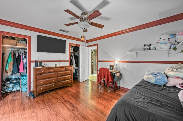 bedroom with crown molding, ceiling fan, dark hardwood / wood-style floors, and two closets