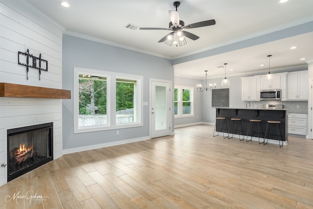 living room with light wood-type flooring, a large fireplace, ceiling fan with notable chandelier, and ornamental molding