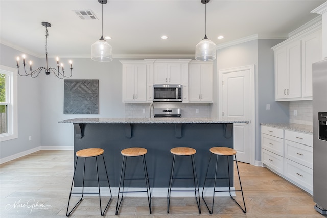 kitchen with appliances with stainless steel finishes, pendant lighting, and an island with sink