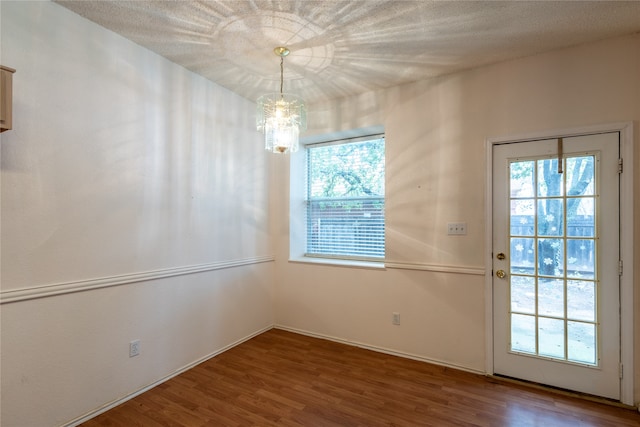 unfurnished dining area with a wealth of natural light, dark hardwood / wood-style floors, an inviting chandelier, and a textured ceiling