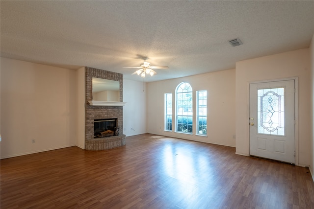 unfurnished living room featuring dark wood-type flooring, ceiling fan, a fireplace, and a textured ceiling