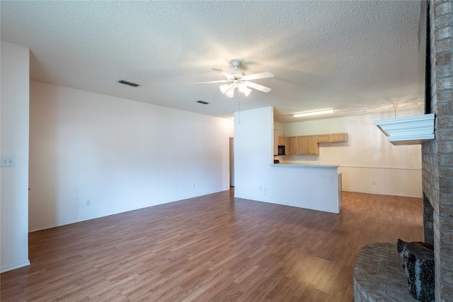 unfurnished living room with a textured ceiling, hardwood / wood-style floors, ceiling fan, and a stone fireplace