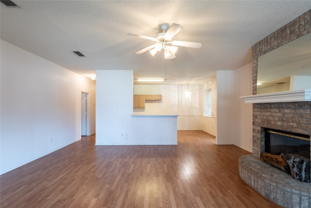 unfurnished living room with dark wood-type flooring, a textured ceiling, a brick fireplace, and ceiling fan