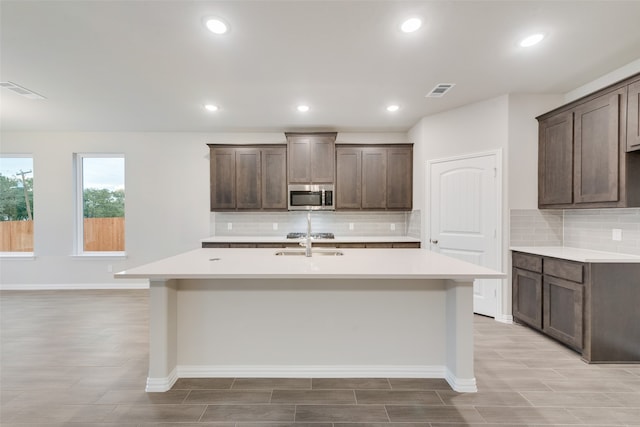 kitchen with dark brown cabinetry, a center island with sink, and tasteful backsplash