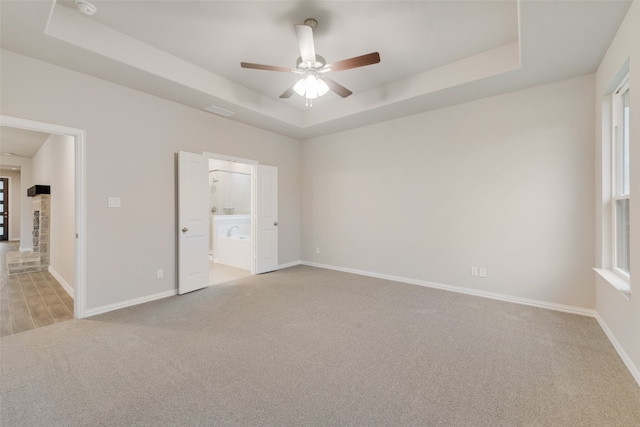 unfurnished bedroom featuring ceiling fan, light colored carpet, ensuite bath, and a raised ceiling