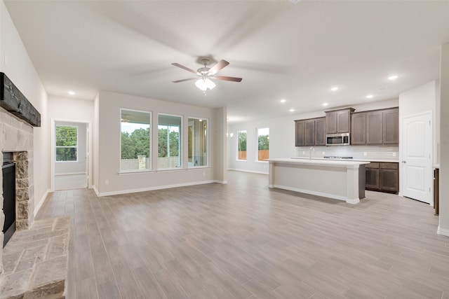 unfurnished living room featuring a fireplace, a wealth of natural light, ceiling fan, and light wood-type flooring