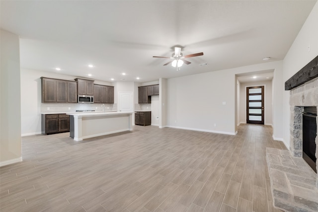 unfurnished living room featuring a stone fireplace, light hardwood / wood-style floors, ceiling fan, and sink