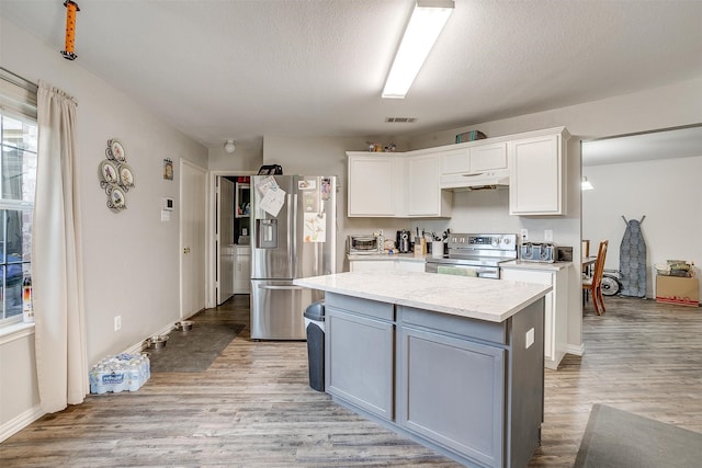 kitchen with appliances with stainless steel finishes, light wood-type flooring, white cabinetry, and a kitchen island