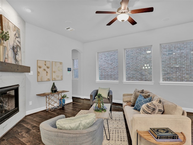 living room with a high end fireplace, ceiling fan, and dark wood-type flooring