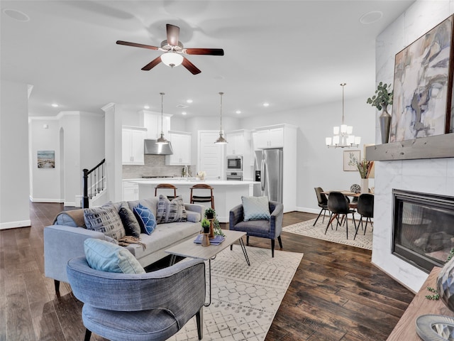 living room with ornamental molding, ceiling fan with notable chandelier, dark wood-type flooring, sink, and a tiled fireplace