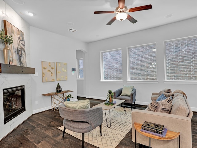 living room featuring ceiling fan, a high end fireplace, and dark wood-type flooring