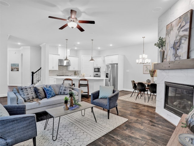 living room featuring a high end fireplace, ceiling fan with notable chandelier, and dark wood-type flooring