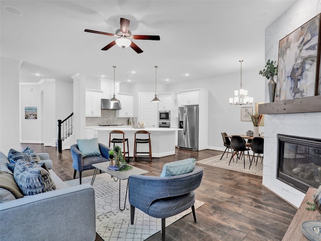 living room featuring a tile fireplace, crown molding, dark wood-type flooring, and ceiling fan with notable chandelier