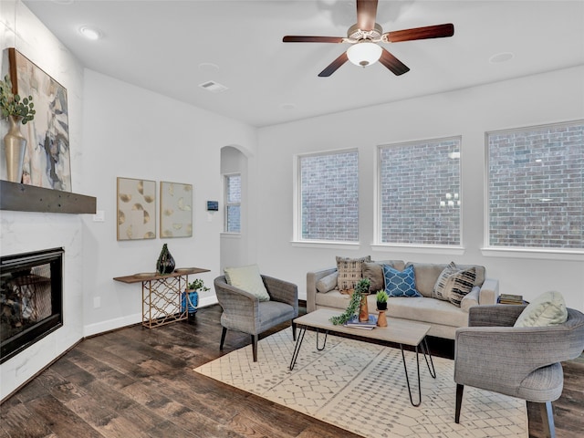 living room featuring a premium fireplace, ceiling fan, and dark wood-type flooring