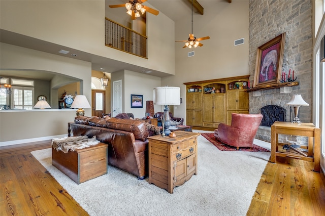 living room featuring a towering ceiling, hardwood / wood-style floors, ceiling fan, and a stone fireplace