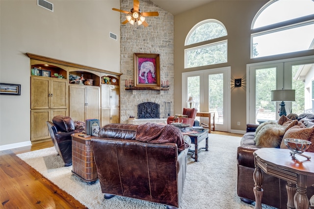 living room featuring a fireplace, light wood-type flooring, high vaulted ceiling, ceiling fan, and french doors