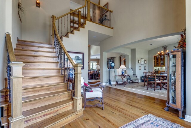 staircase featuring wood-type flooring, a notable chandelier, and a towering ceiling