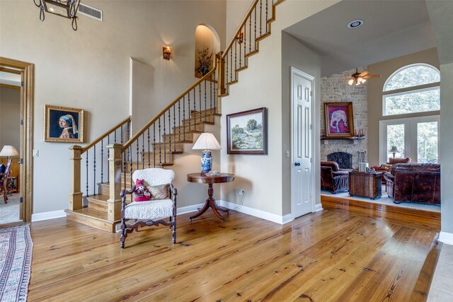 interior space featuring light wood-type flooring, a towering ceiling, and a stone fireplace